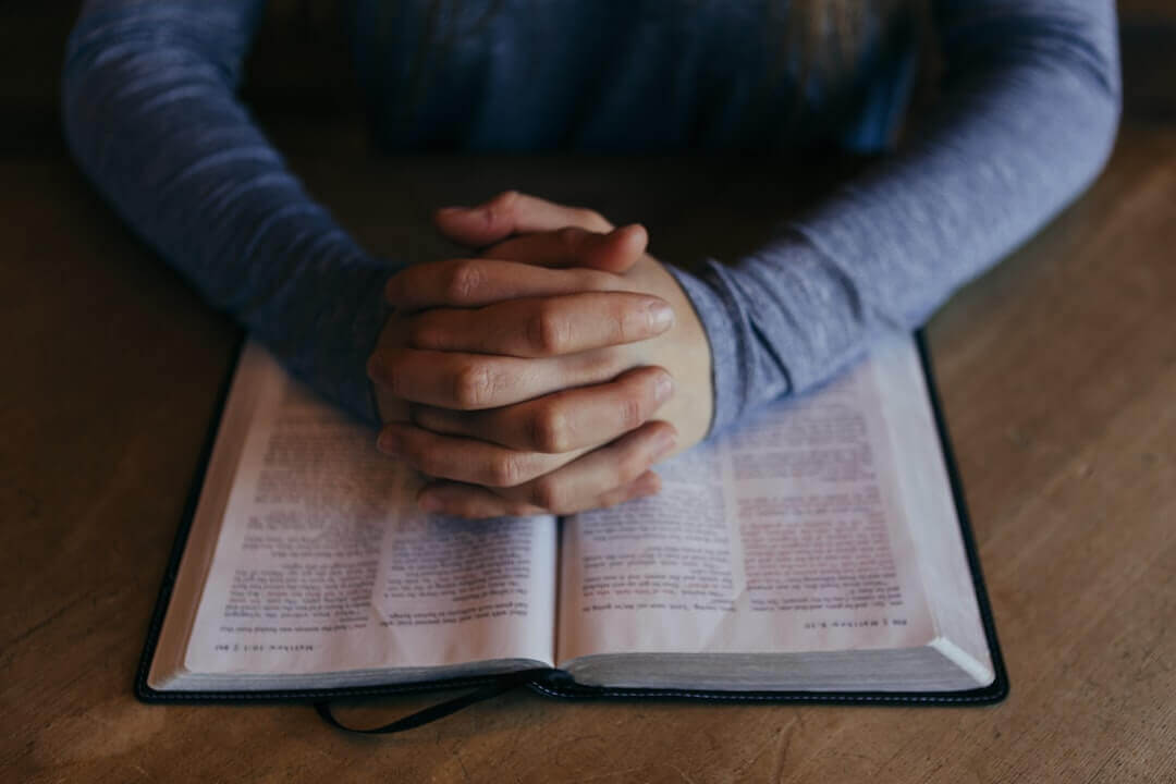 Man praying with his hands on the Bible.
